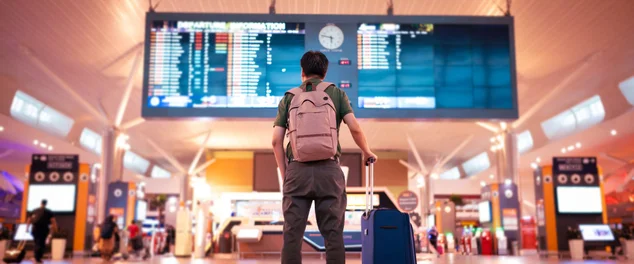 homem no aeroporto com mala olhando para telão
