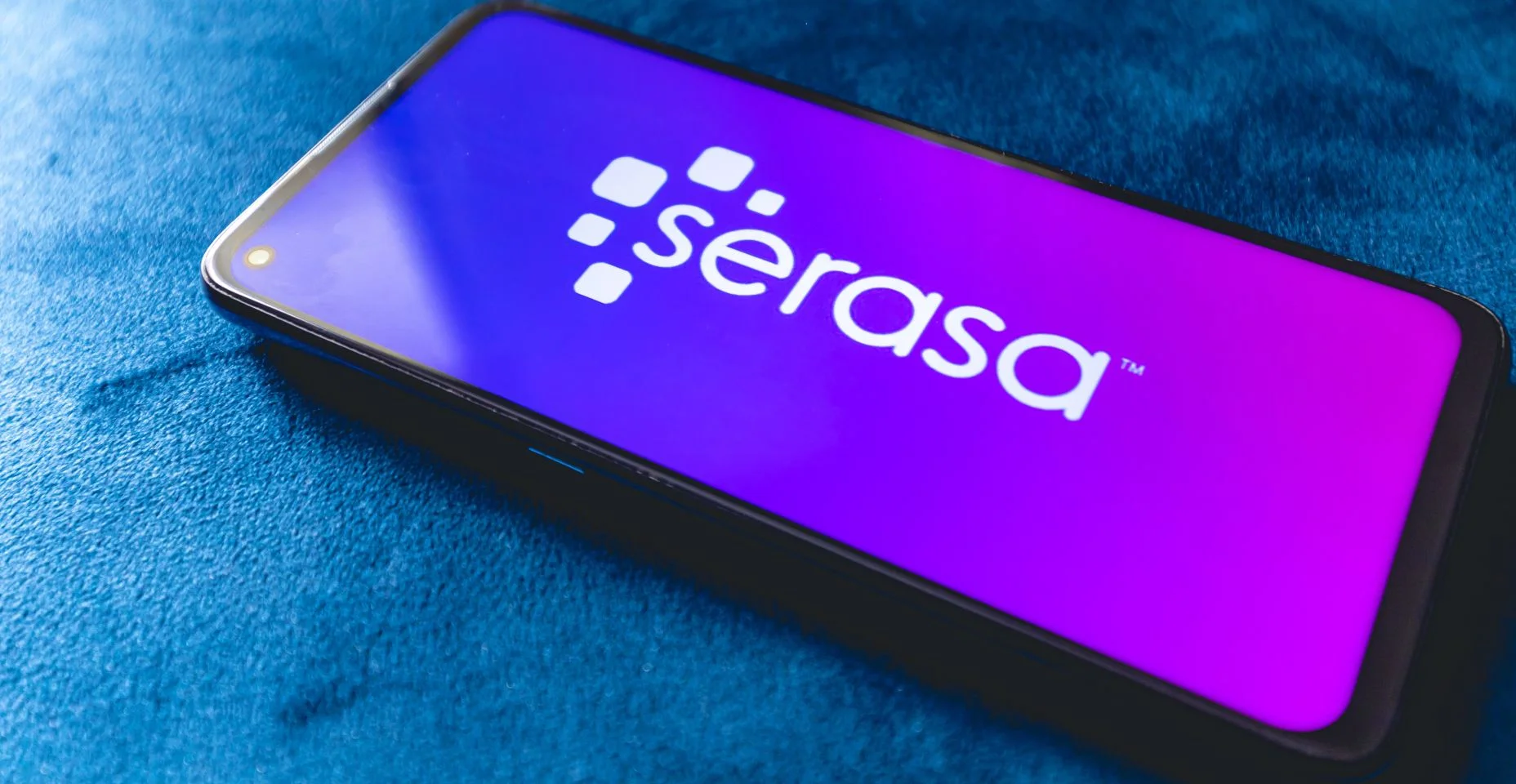 Um telefone celular com a logo da empresa brasileira Serasa sobre um sofá azul.