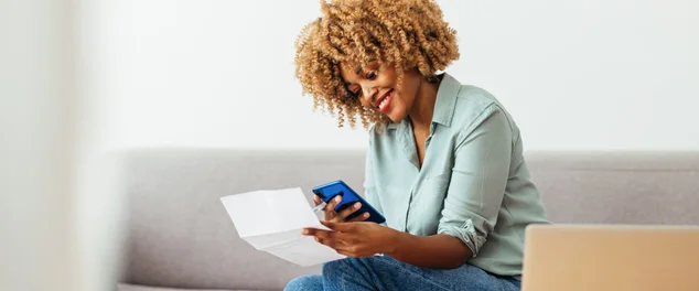 Mulher negra sentada no sofá pesquisando no celular como fazer empréstimo na conta de luz