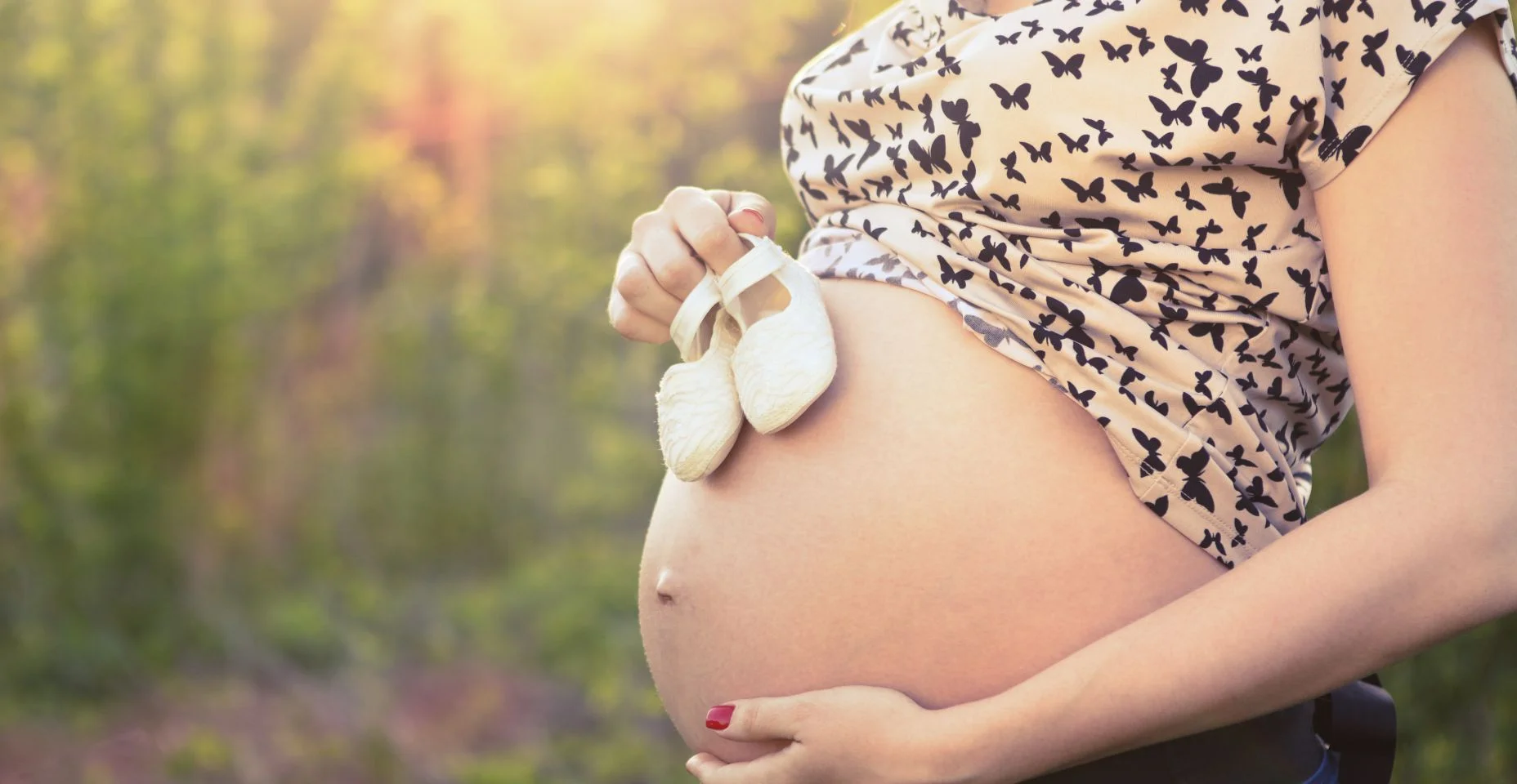 Close-up de mulher grávida irreconhecível com sapatos de bebê