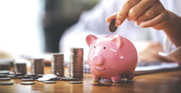 Empresário segurando uma moeda em um cofrinho em uma mesa com luz solar. Ideias de economia de dinheiro para contabilidade financeira