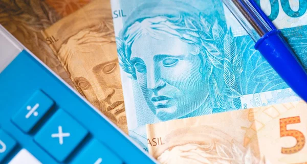 Uma calculadora, notas de reais e uma caneta.
