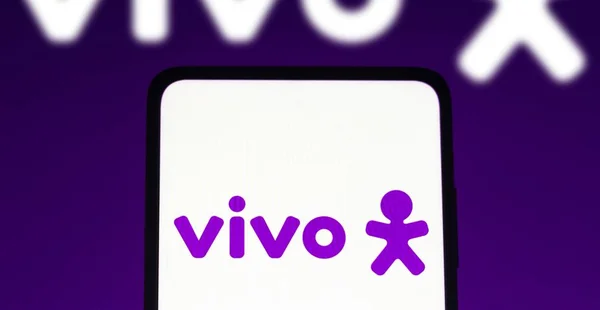 Nesta ilustração fotográfica o logotipo da Vivo visto exibido em um smartphone e no fundo.