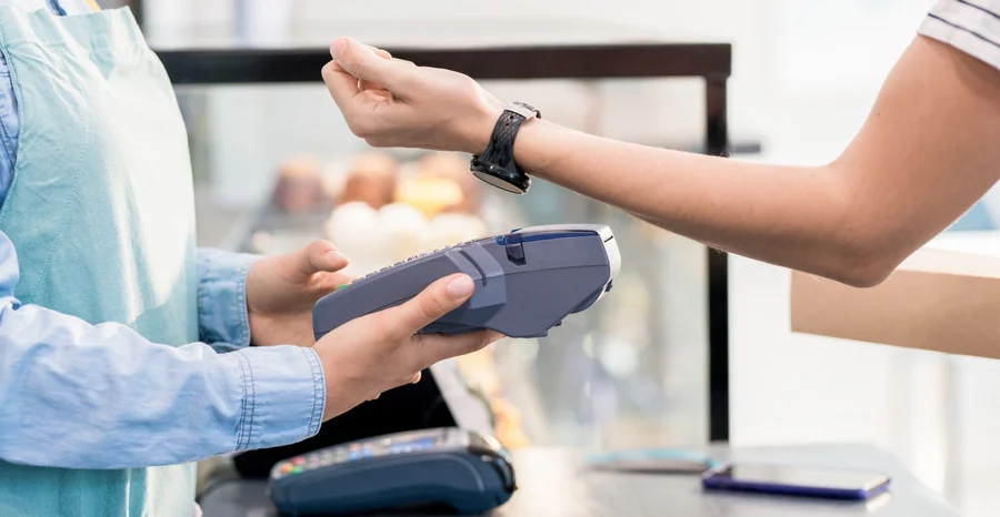 Vista lateral da seção intermediária de uma mulher irreconhecível pagando por relógio inteligente via NFC seu pedido em uma loja ou café