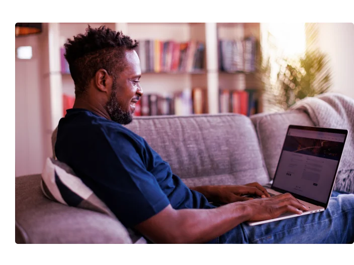 Homem sorridente relaxado sentado no sofá e usando laptop