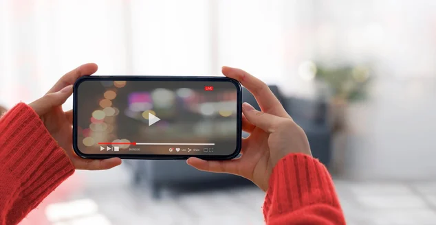 Mulher segurando e assistindo vídeo via celular na visão horizontal em casa.