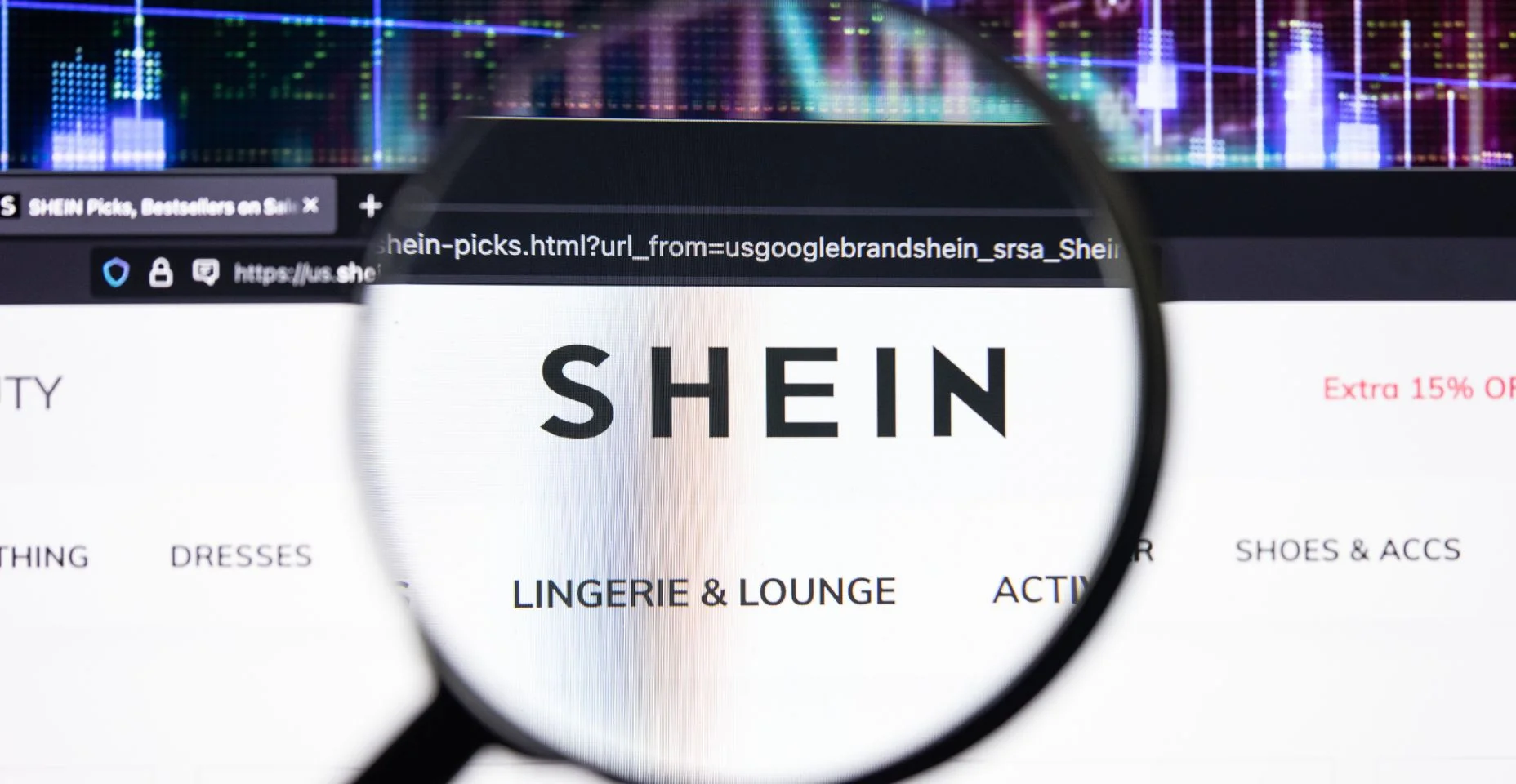 Logotipo da empresa SHEIN em um site com desenvolvimentos desfocados do mercado de ações em segundo plano, visto na tela de um computador através de uma lupa