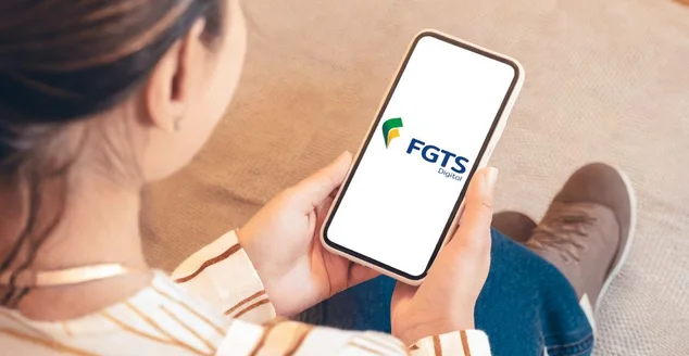 Uma mulher adulta irreconhecível em sua sala segurando seu smartphone com o logotipo do FGTS Digital na tela do telefone.