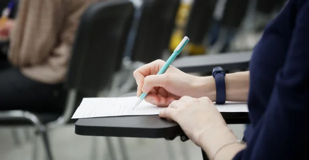 Uma garota escreve um ditado ou preenche documentos na plateia, sentada em uma cadeira da escola com uma banca de escrita.