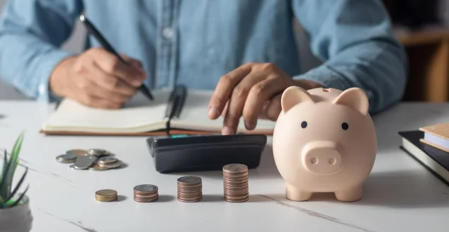 Homem colocando moeda em cofrinho e pressionar a calculadora com moedas colocadas no livro de contas conceito de economia de dinheiro