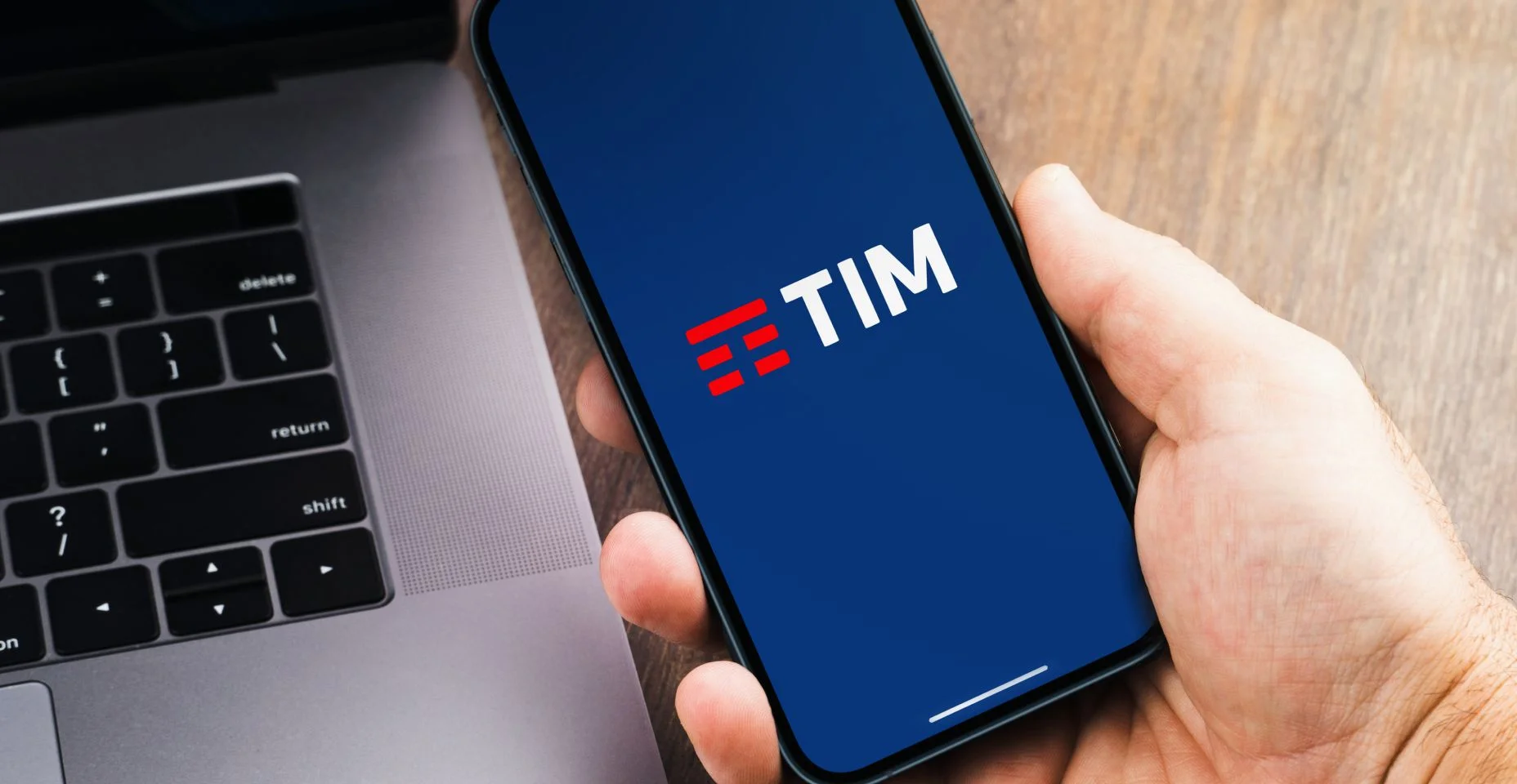 Mão masculina segurando um smartphone com Tim, empresa de telecomunicações, aplicativo na tela.