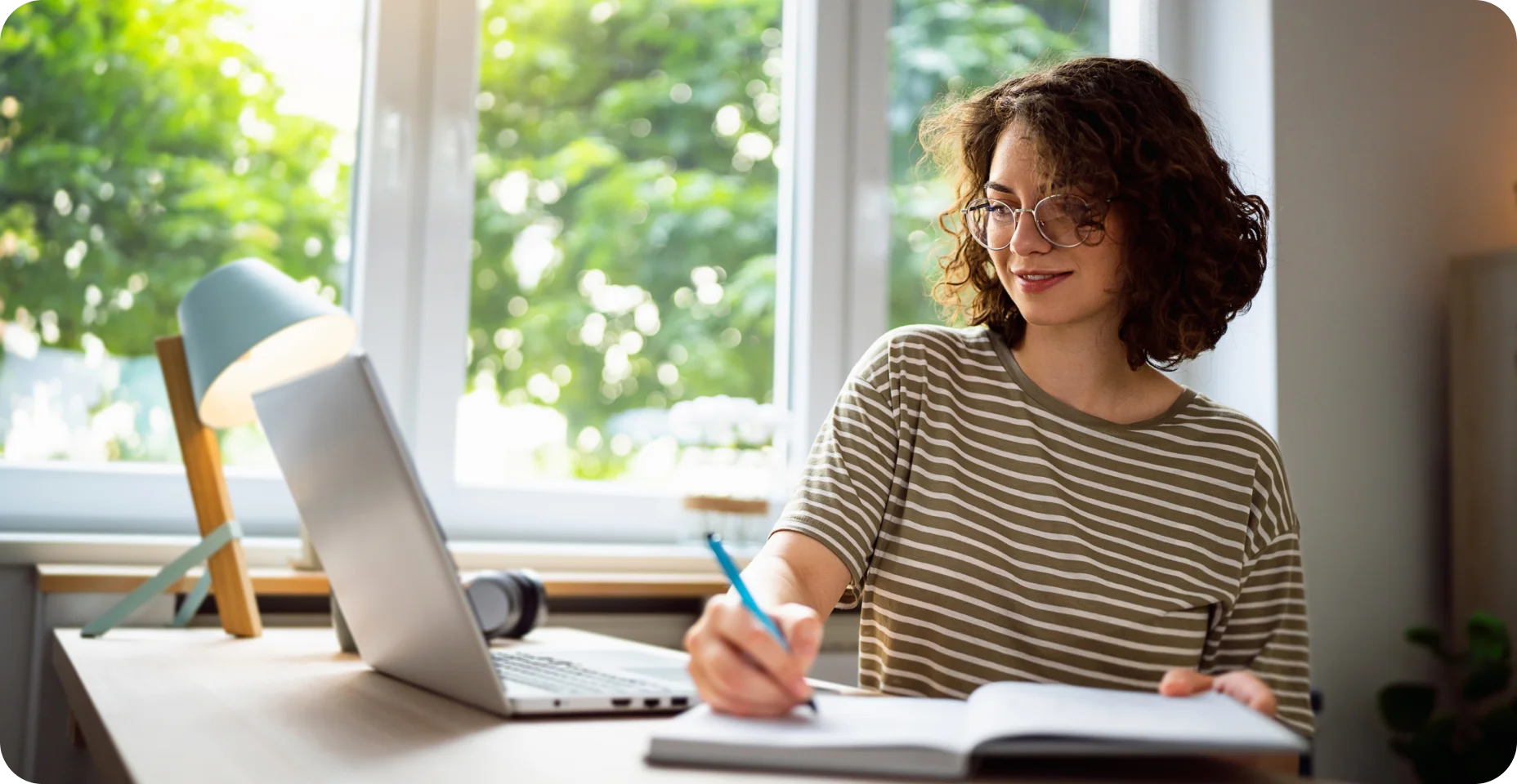 Mulher olhando para o notebook e fazendo anotações em seu caderno