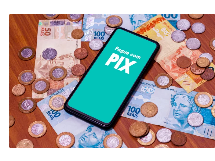 Celular com logo do pix encima de moedas e cédulas