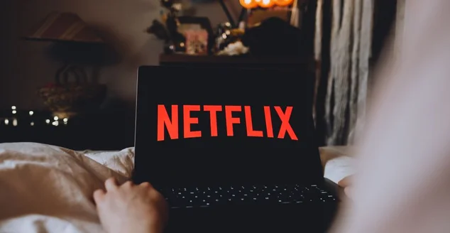 Logotipo da Netflix na tela do laptop. Jovem assistindo canal netflix sentada em casa à noite.