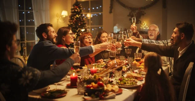 Retrato de um belo jovem negro propondo um brinde em uma mesa de jantar de Natal. Família e amigos compartilhando refeições, levantando taças com champanhe, brindando, celebrando um feriado de inverno