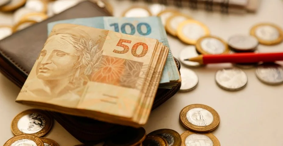 Notas de cinquenta reais e outras notas e moedas sobre a mesa com carteira, lápis e caderno