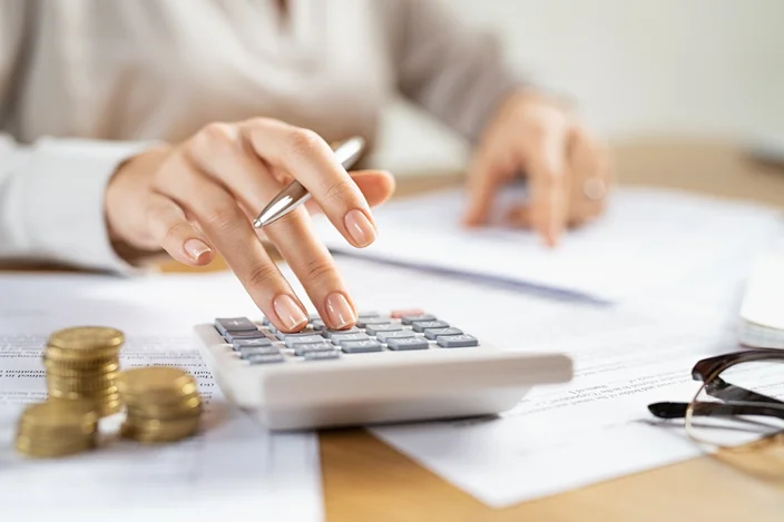 mão de uma mulher fazendo cálculo numa calculadora com uma caneta na mão.