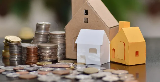 Casa de papel e pilhas de moedas em pé