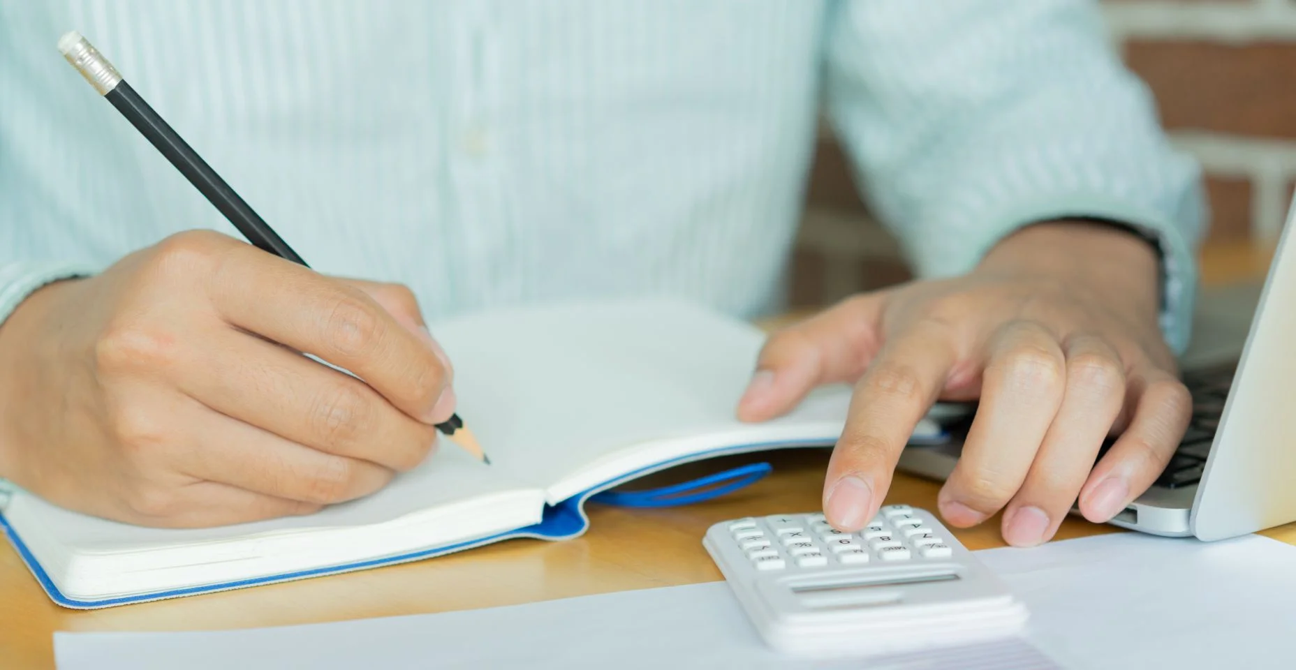 Fechar em mão homem escrever em notebook e calcular na calculadora sobre pagamento de dívida mensalmente na mesa para conceito de gestão de dinheiro
