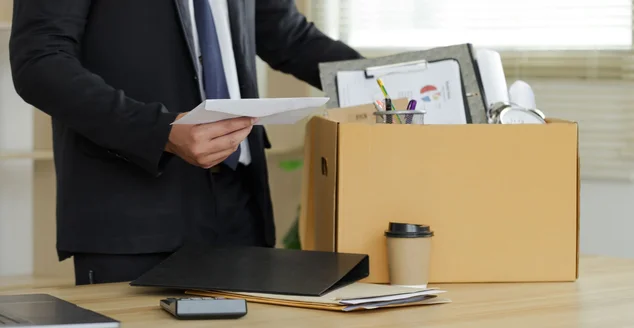 O empresário coloca sua caixa de sua parte na mesa e segura a carta branca. Largando um emprego, um homem de negócios demitiu ou deixou um conceito de emprego. A grande renúncia.