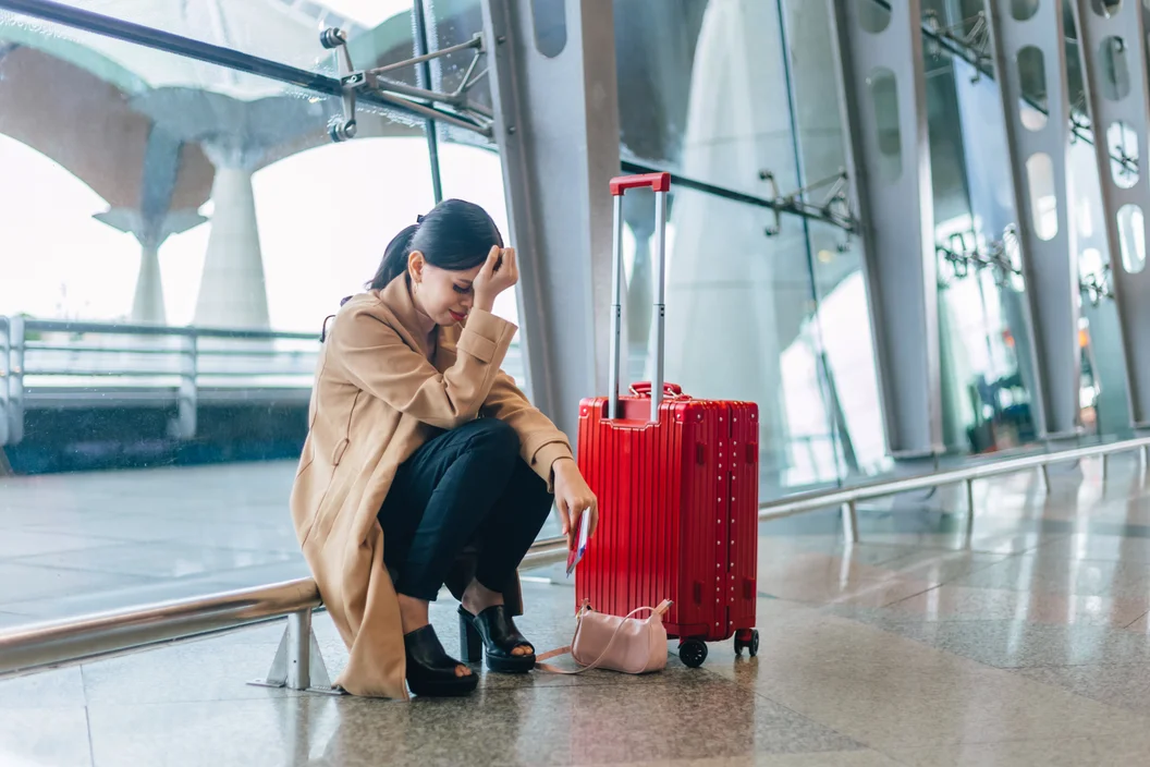 Mulher ajoelhada no chão do aeroporto chorando ao lado de sua mala