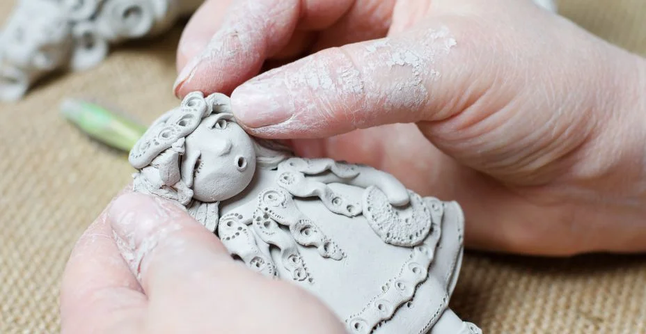 O processo de fazer uma boneca de lembrança feita de argila. Mãos fêmeas que prendem um brinquedo feito da argila.