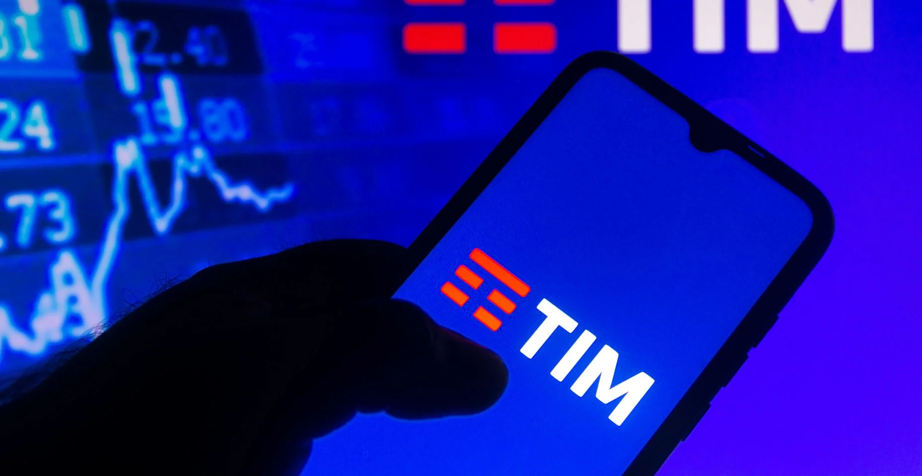Nesta ilustração fotográfica o logotipo da TIM visto exibido em um smartphone com as informações do mercado de ações ao fundo.