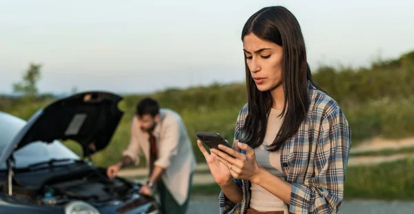 Casal com avaria do veículo e usando o telefone para ligar para o seguro do carro