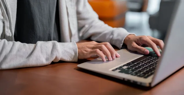 Uma imagem em close-up de um homem asiático com roupas confortáveis trabalhando em seu laptop, trabalhando dentro de casa.