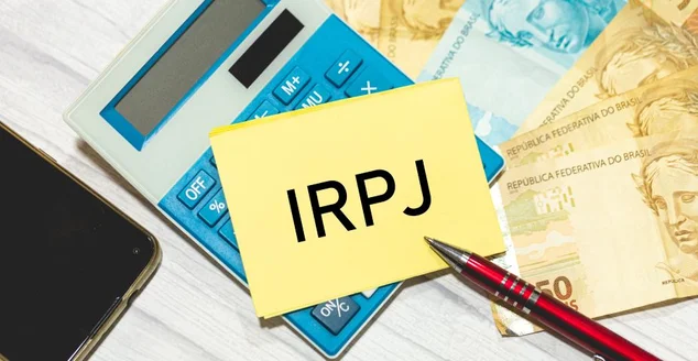 A sigla IRPJ referente ao Imposto sobre a renda das pessoas jurídicas escrita em um pedaço de papel que está sobre uma calculadora. Notas do Real Brasileiro na composição. Economia brasileira.