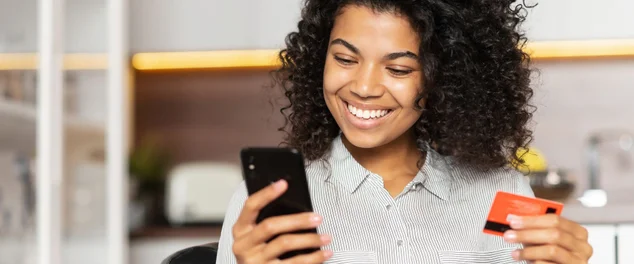 Mulher olhando seu celular com um cartão na mão para ilustrar artigo sobre cartões pré-pagos