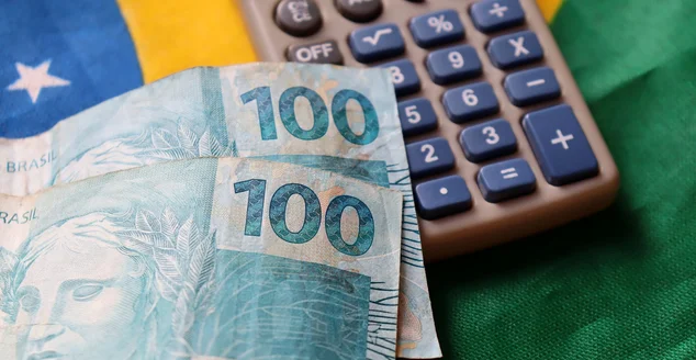 Notas reais e calculadora em cima da bandeira do Brasil. Conceito de finanças e economia