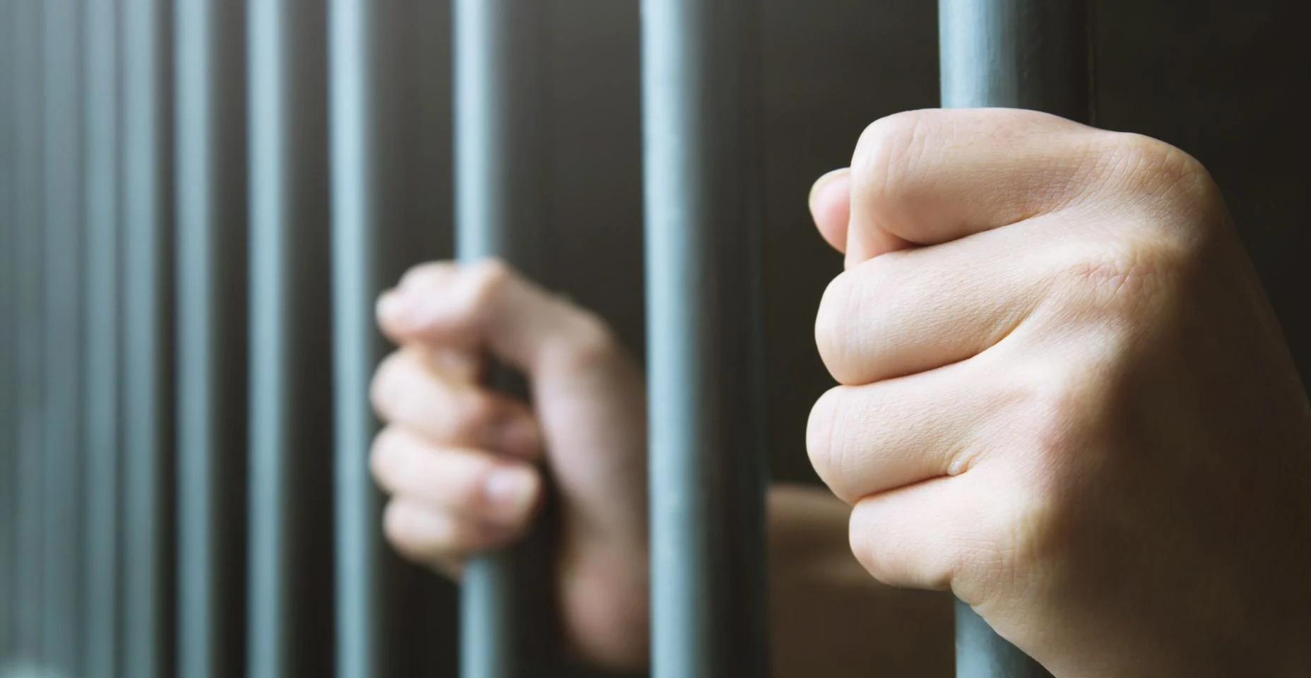 Homem na prisão mãos de atrás espera gaiola de aço barras de prisão. penal do ofensor trancado na cadeia