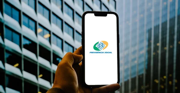 pessoa segurando um celular com o app do Meu INSS, com o fundo cheio de prédio