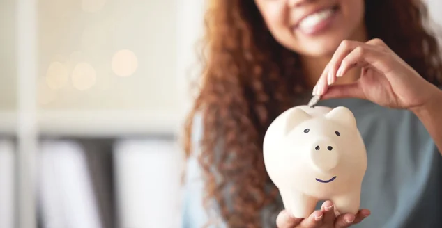 Uma jovem mestiça feliz segurando um cofrinho e depositando uma moeda como poupança. Mulher hispânica orçando suas finanças e investindo dinheiro em seu futuro. Economizando fundos para a liberdade financeira