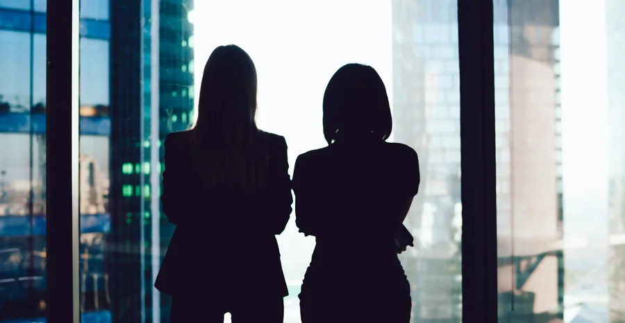 Visão de trás de colegas mulheres em desgaste formal em pé perto da janela olhando para o exterior moderno de arranha-céus no centro de negócios, silhueta de mulheres juntas planejando sucesso futuro de brainstorming