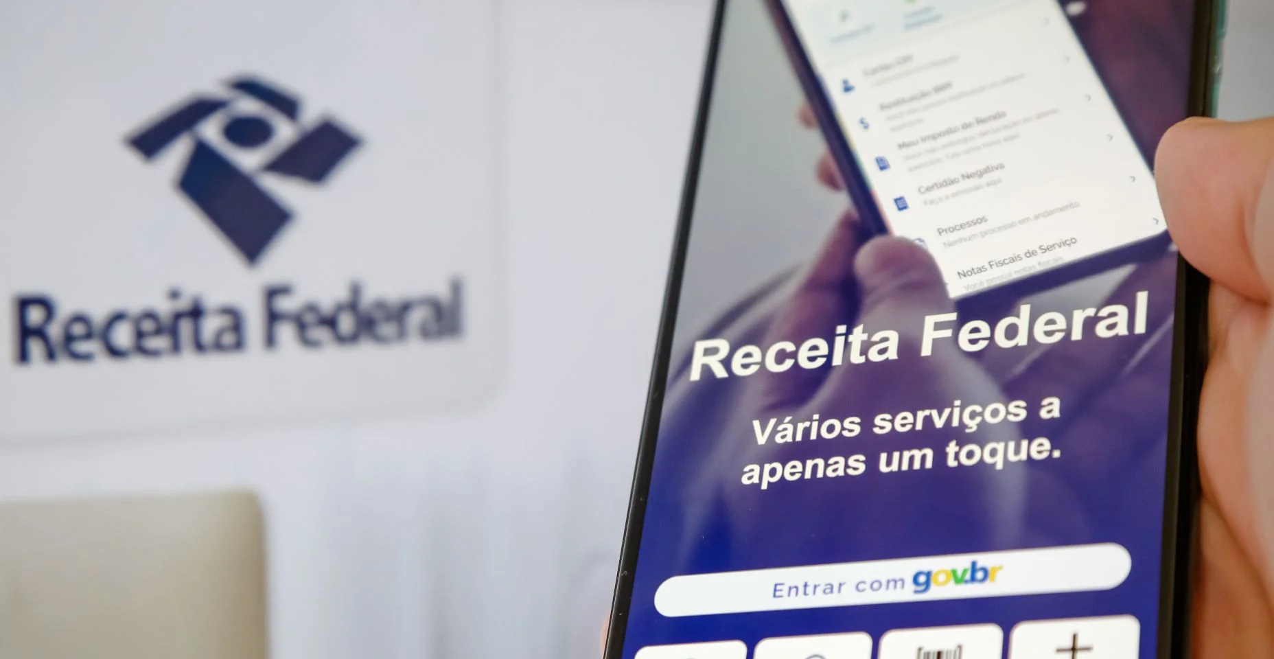 Imposto de renda 2024 da receita federal segurando celular com aplicativo e dinheiro