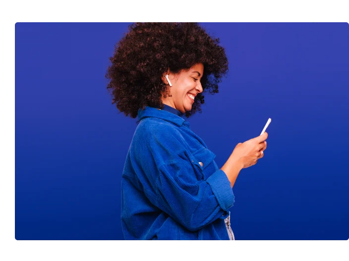 Mulher em um fundo azul, olhando para o celular e sorrindo