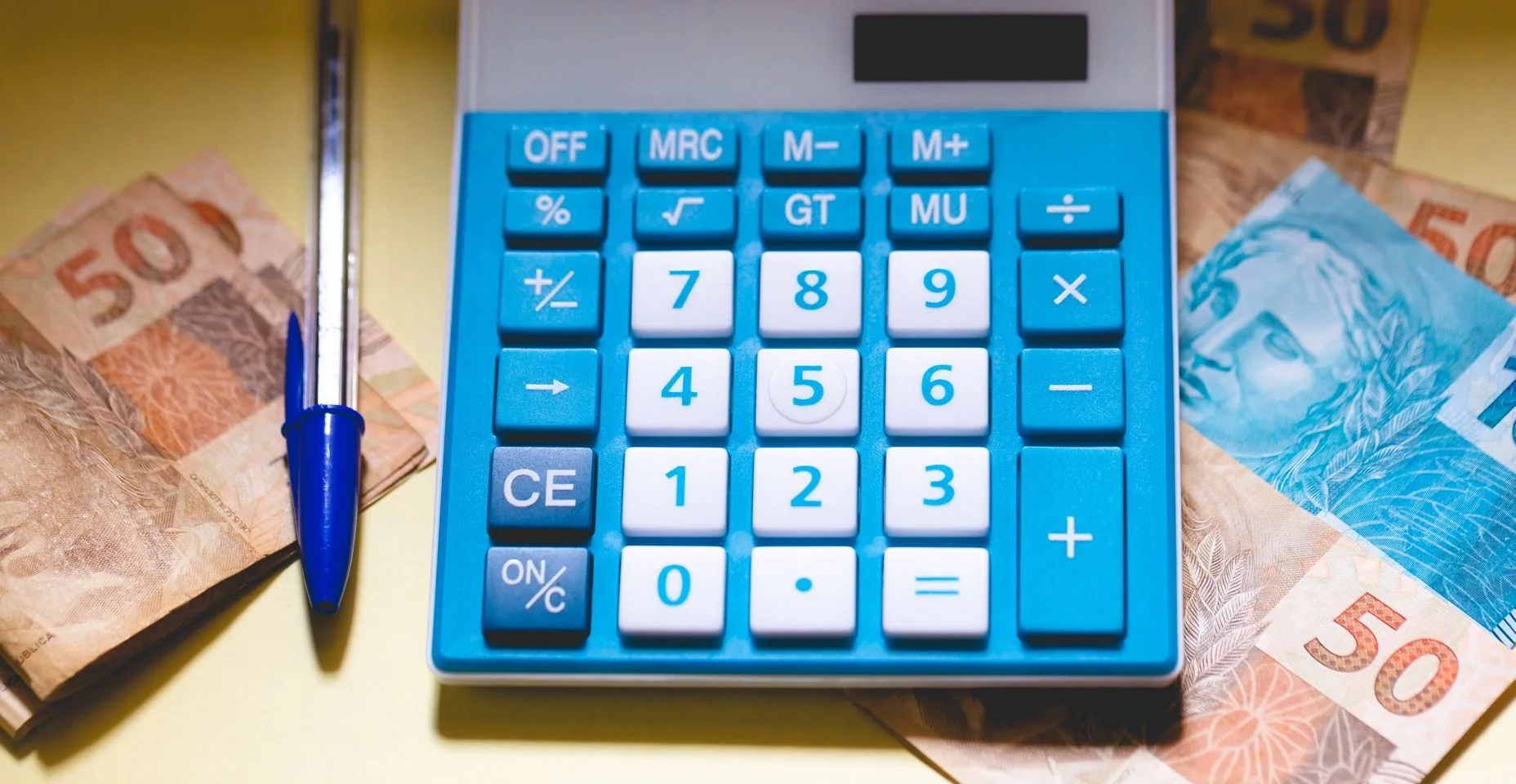 Uma calculadora, notas de reais e uma caneta. Economia e finanças brasileiras.
