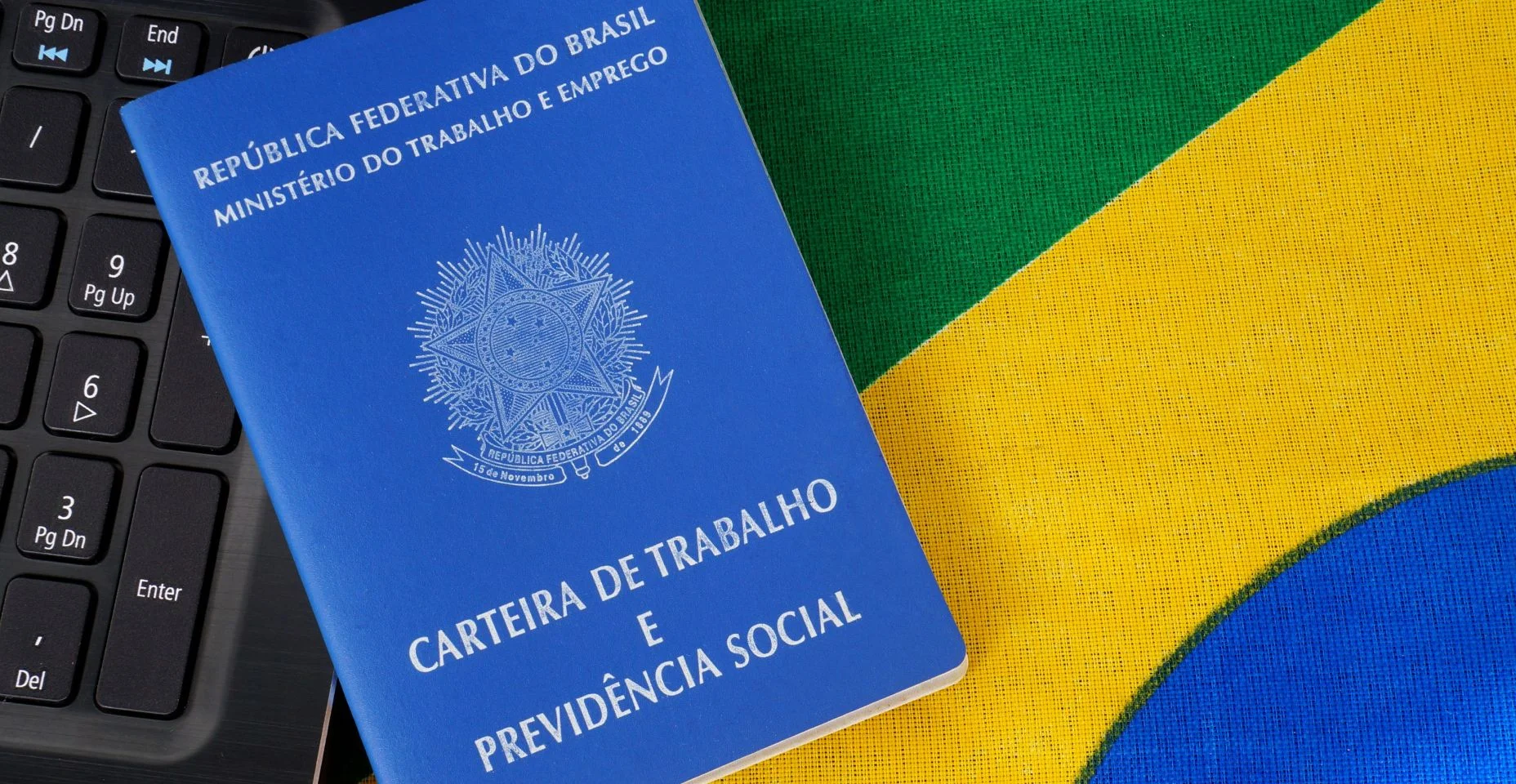 carteira de trabalho e laptop em cima da bandeira brasileira.