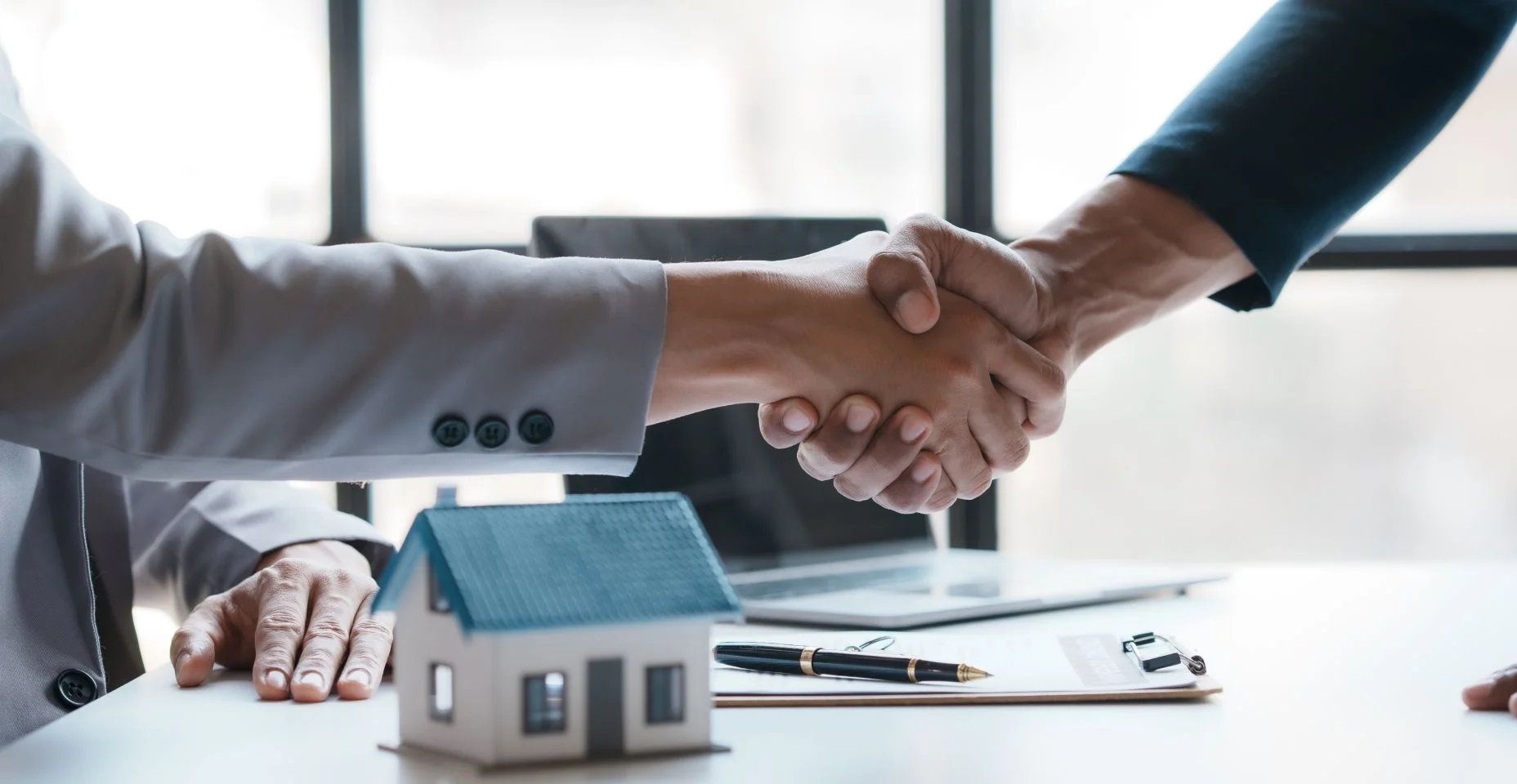 Imobiliária aperta a mão de um cliente para assinar um contrato de compra de casa parabenizando o cliente pela compra.