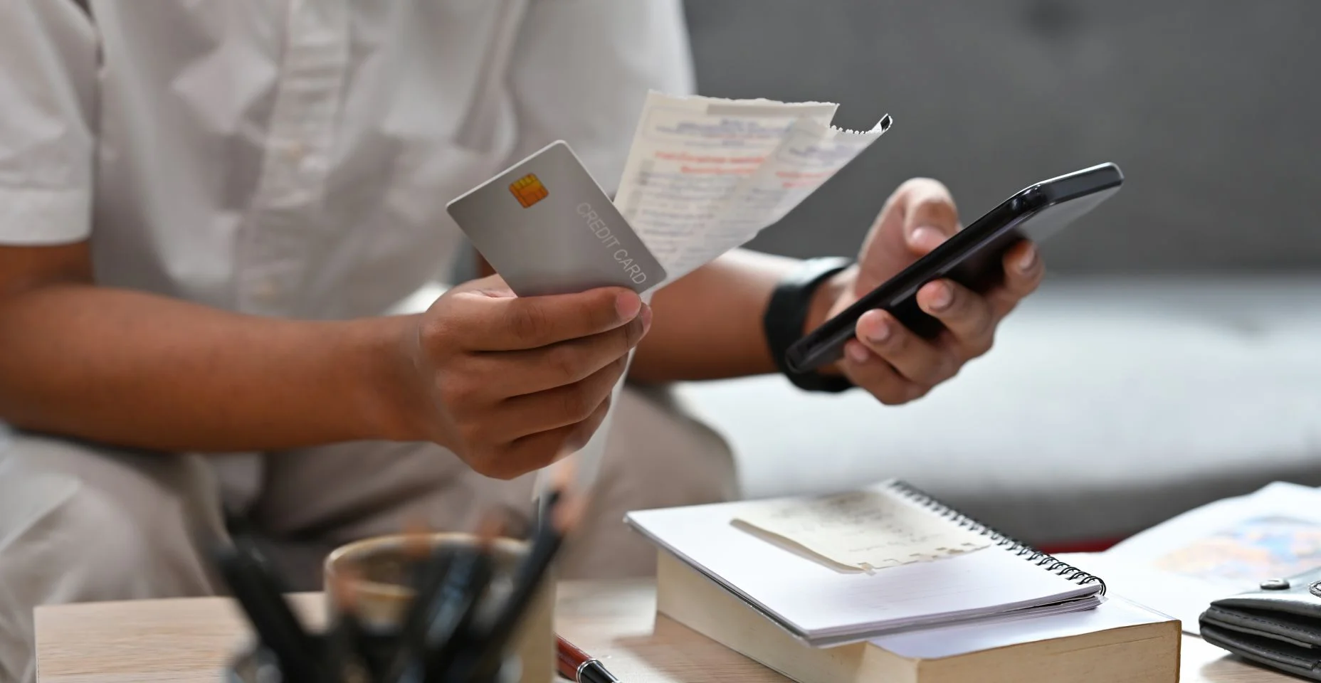 Feche com o homem sentado em um sofá enquanto segura contas e cartão de crédito e usando o celular para calcular, finanças, negócios, casa e conceito de tecnologia.