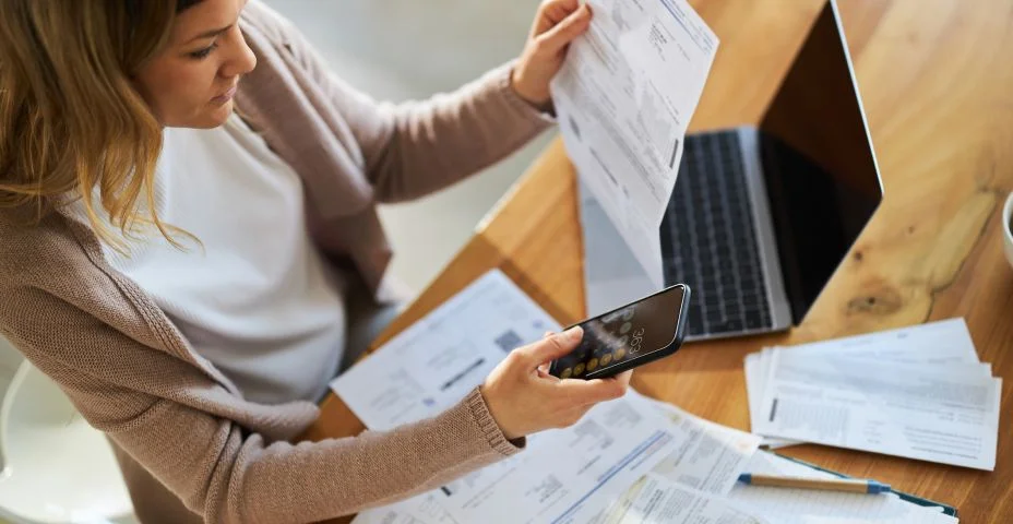 Vista acima de uma mulher usando o telefone celular enquanto calcula as finanças da casa.