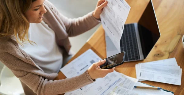 Vista acima de uma mulher usando o telefone celular enquanto calcula as finanças da casa.