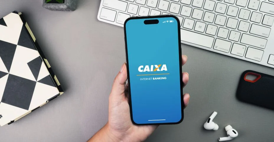 Menina segurando um smartphone com o aplicativo do banco Caixa Econômica Federal na tela da mesa com fundo cinza. Ambiente de escritório.