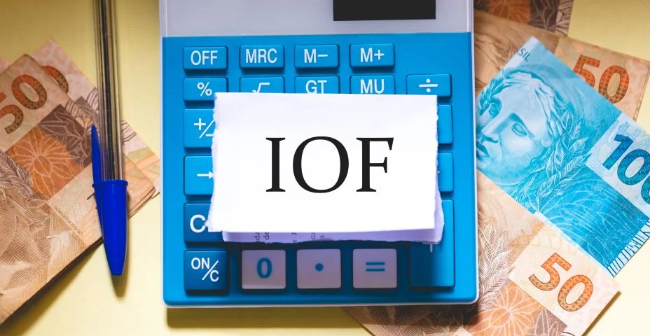 A sigla IOF em Português do Brasil escrita em um pedaço de papel que está sobre uma calculadora. Notas do Real Brasileiro na composição. Economia Brasileira.