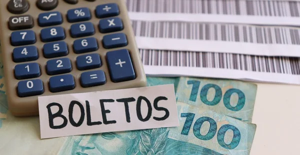 Inscrição boletos em cima de calculadora e cédulas reais brasileiras com notas de código de barras em segundo plano.