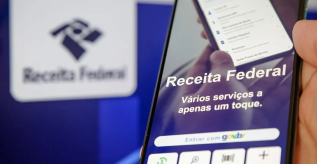 Imposto de renda 2024 da receita federal segurando celular com aplicativo e dinheiro