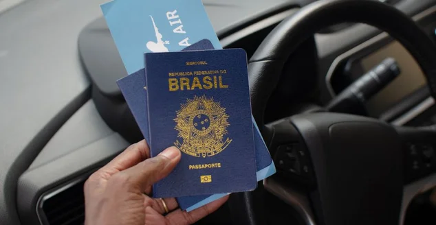 Mão segurando o passaporte brasileiro em um close-up, simbolizando a viagem e a identidade nacional.