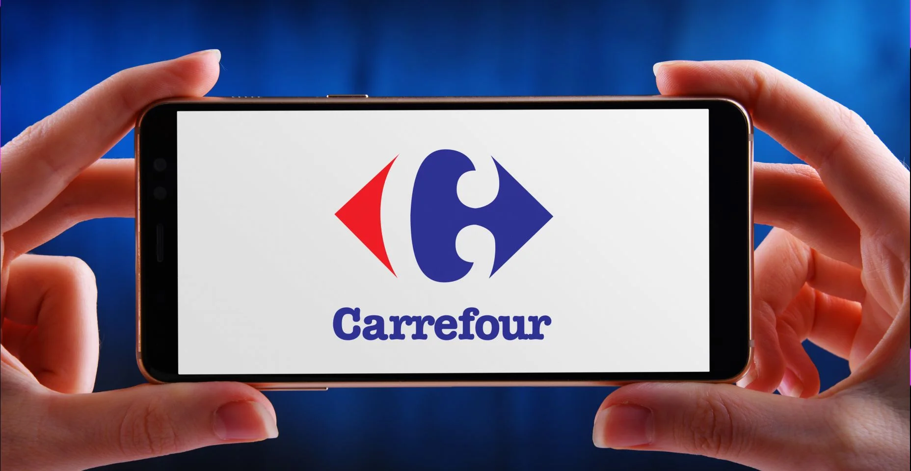 Mãos segurando um smartphone exibindo o logotipo do Carrefour